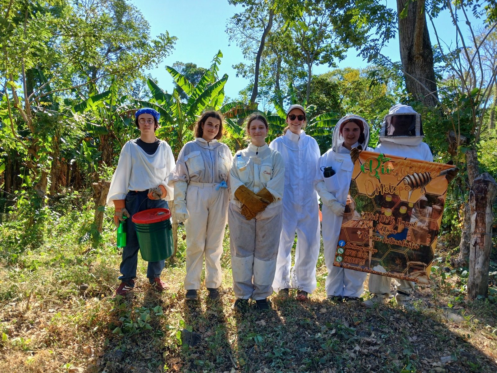 A group of visitors in full beekeeper suits standing with a local beekeeper among tropical trees on Ometepe Island