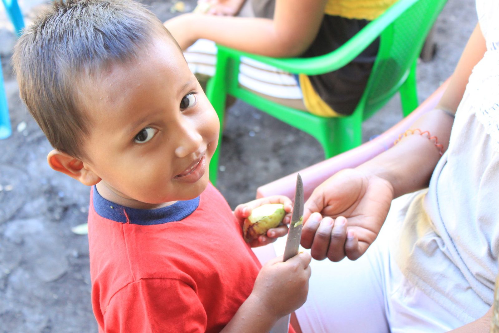 A young boy from the community smiling while being handed a piece of fresh fruit