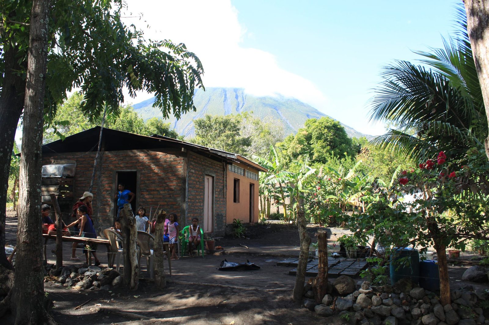 A family homestead in Los Ramos with children playing in the yard and Ometepe's volcano rising behind the house