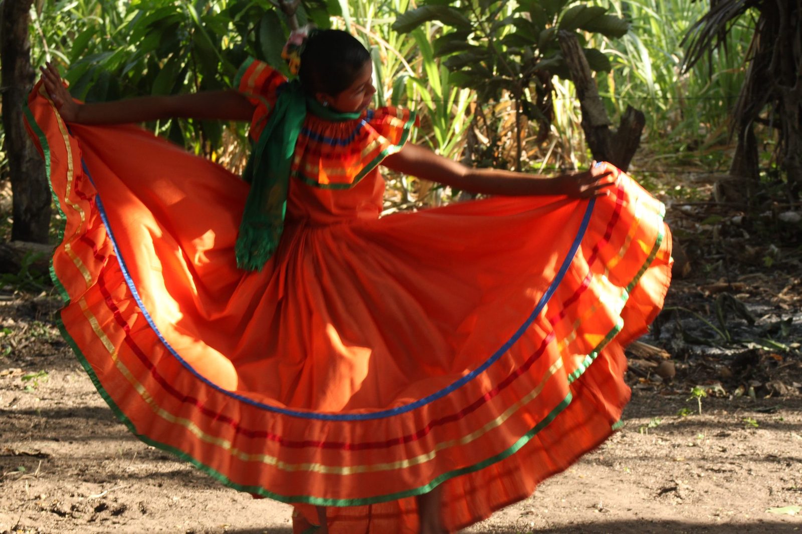 A dancer in a vibrant flowing red and orange traditional dress performing among tropical trees
