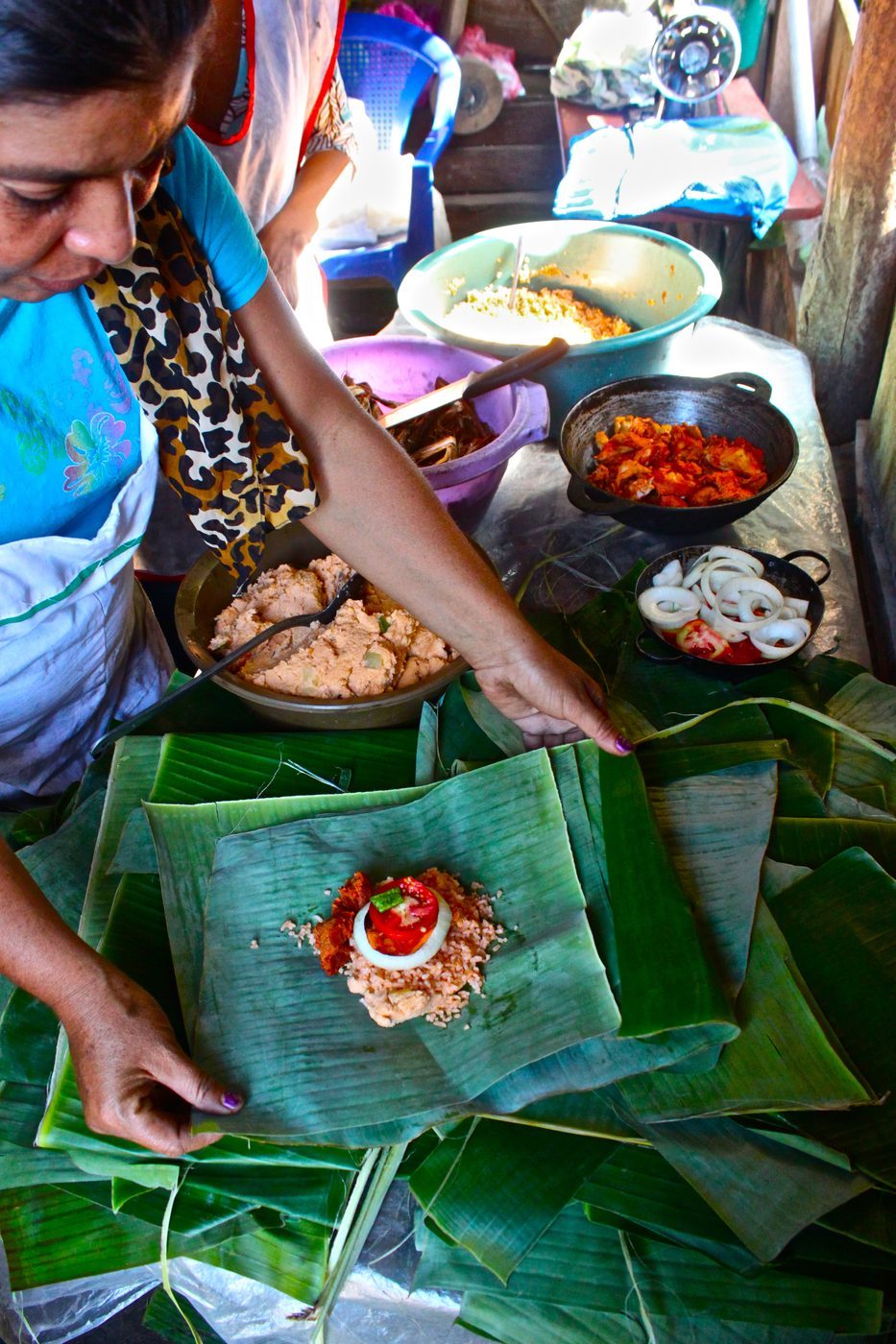 Hands carefully folding banana leaves around nacatamal filling