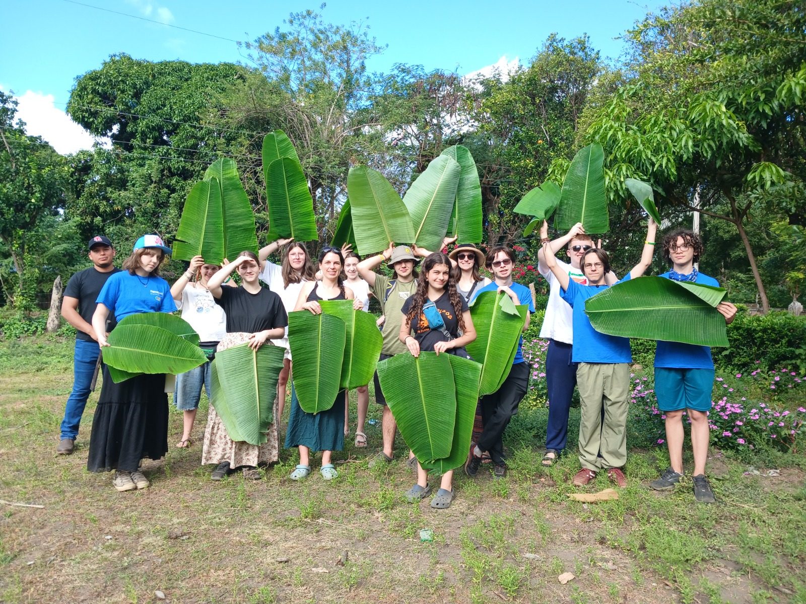 A group of visitors holding freshly cut banana leaves outdoors during a cooking class in Los Ramos