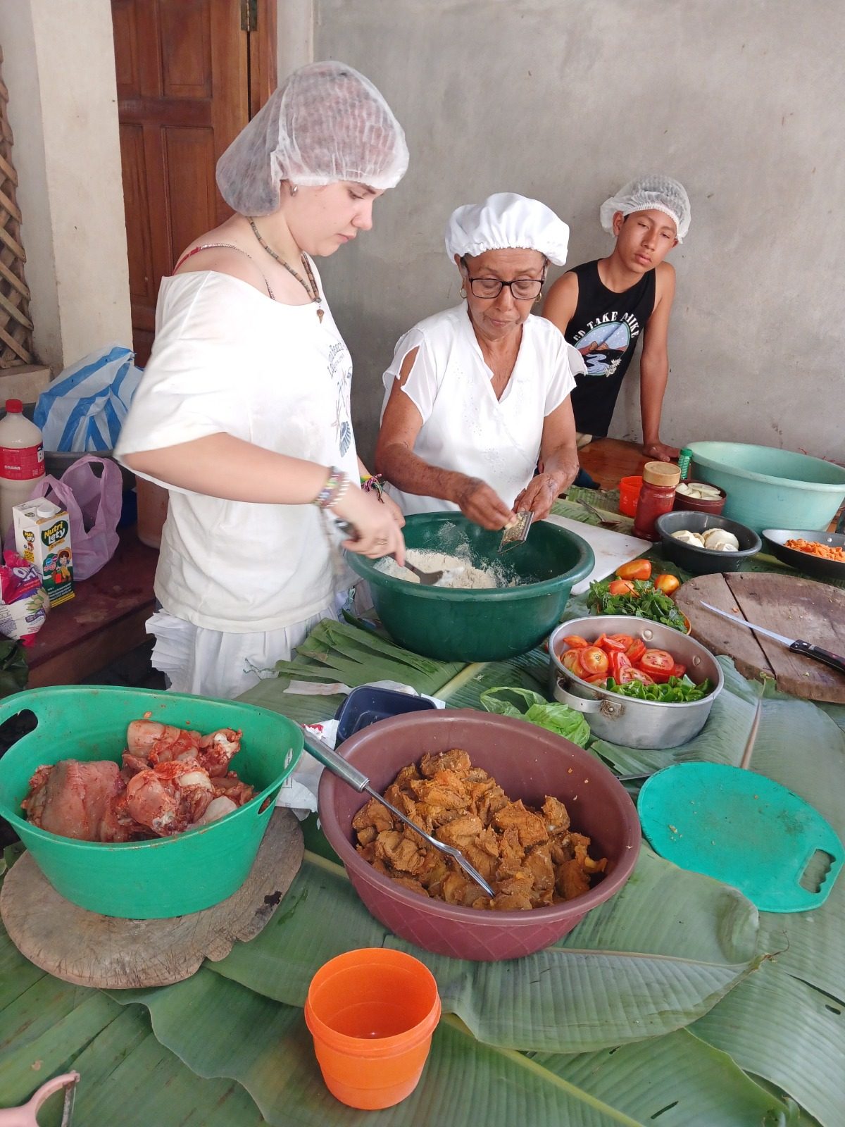 Local women and a visitor preparing nacatamal ingredients together on banana leaves in a traditional kitchen