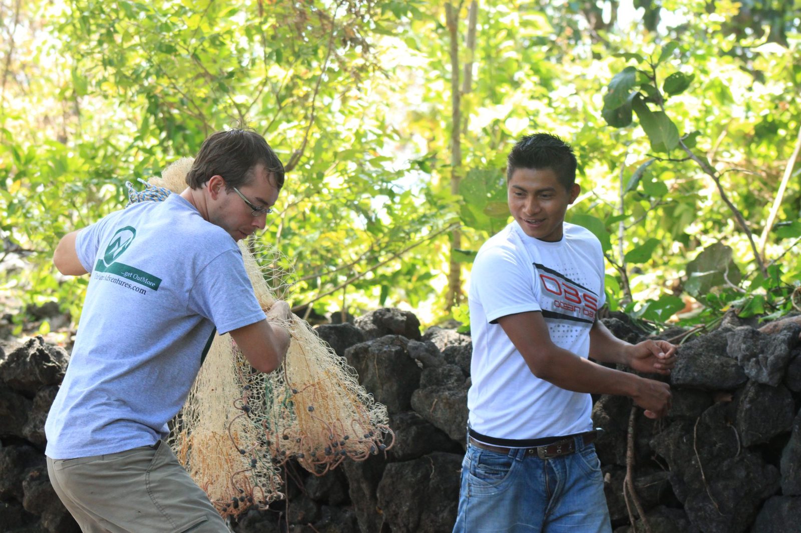 Two men working together with fishing nets near a stone wall