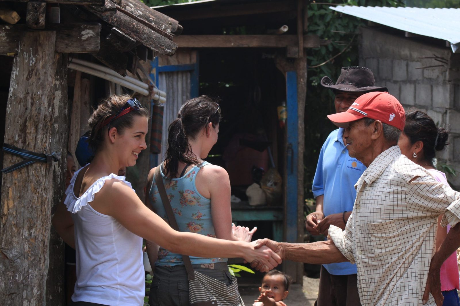 A visitor warmly shaking hands with a community elder while others look on